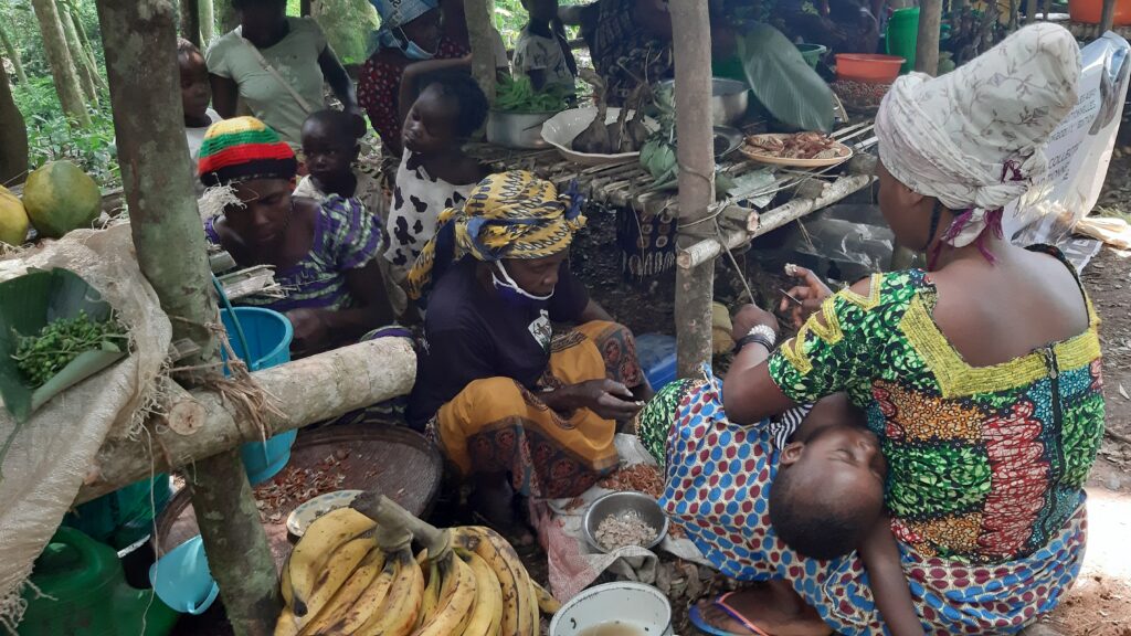 People working while sitting on the ground. One of the person has a baby on her lap.