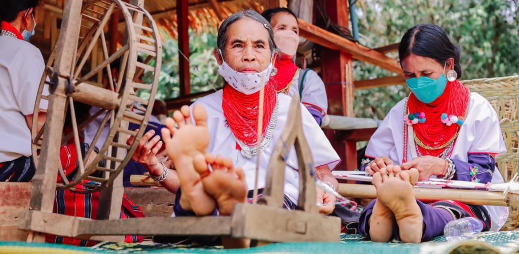 People using Charkha outdoors to make yarn.
